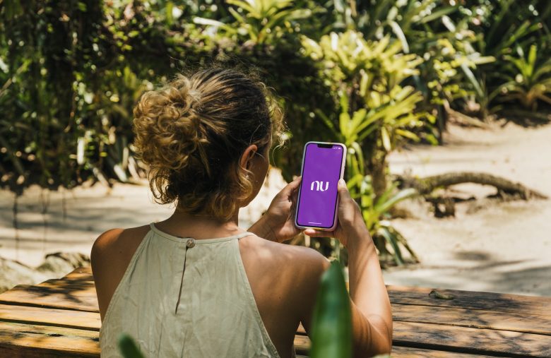 Girl in the park holding a smartphone with Nubank app on the scr