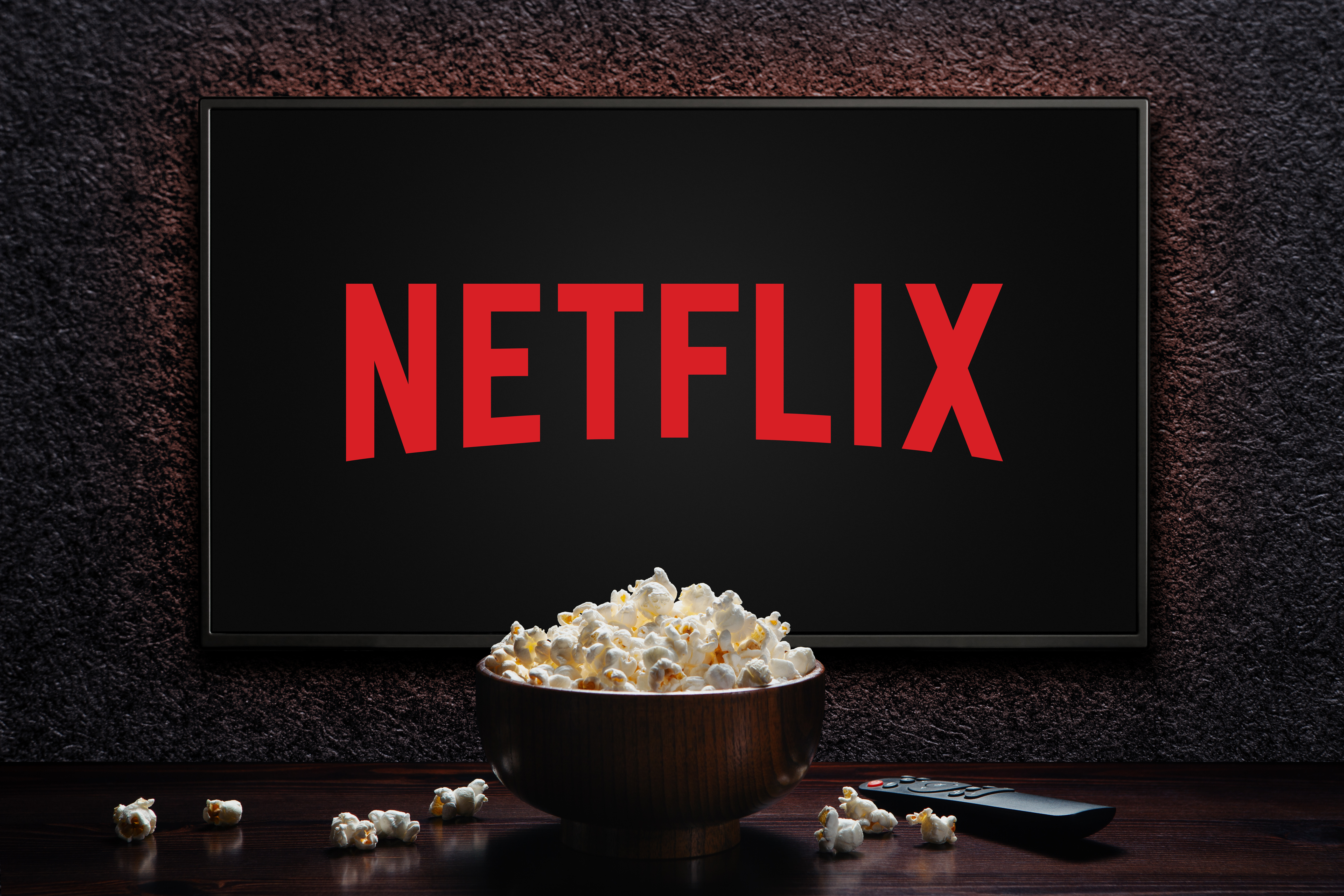 Netflix logo on TV with popcorn bowl and reomote control on the table. Moscow, Russia - November 29, 2022.