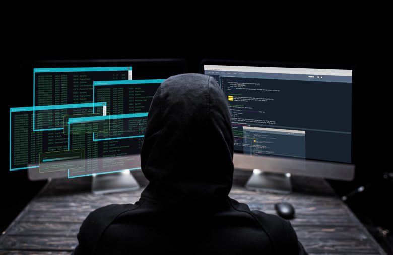 back view of hooded hacker sitting near computer monitors with d
