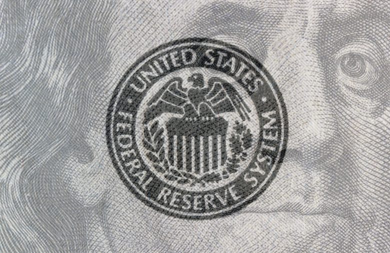Federal Reserve System seal overlay on a hundred dollar bill. The Fed's responsibilities include setting interest rates and regulating financial markets.